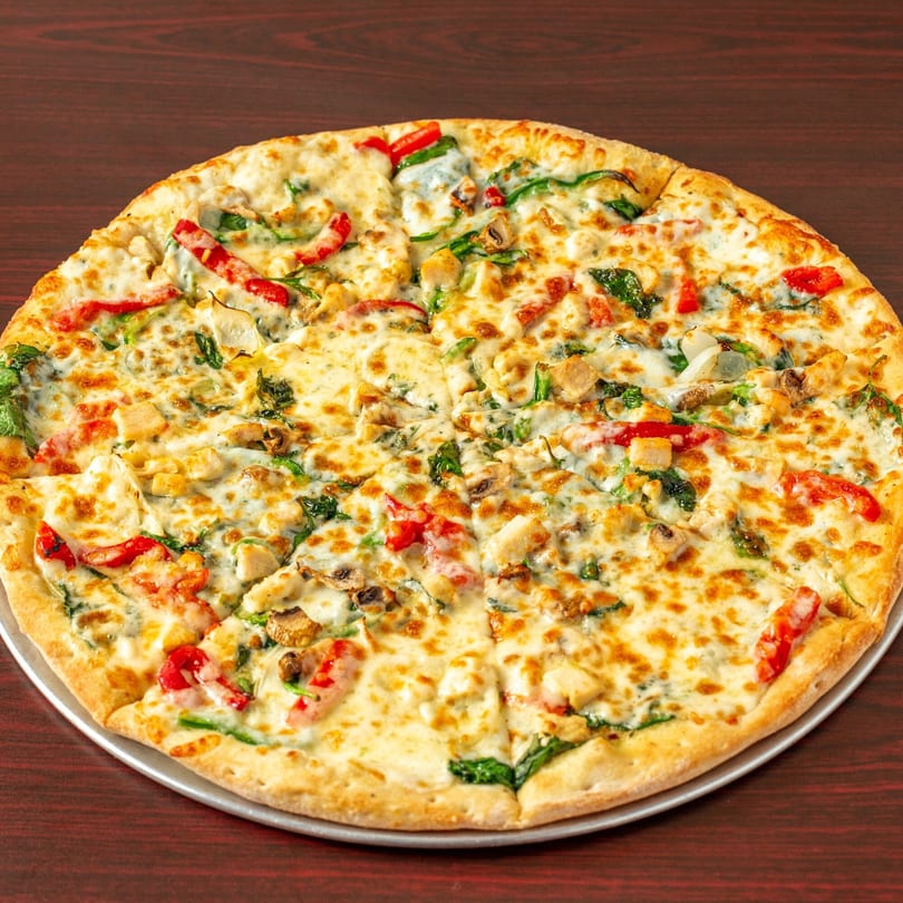 Topolino's pizza with white sauce, chicken, red peppers, spinach, and mushrooms on a dark table.