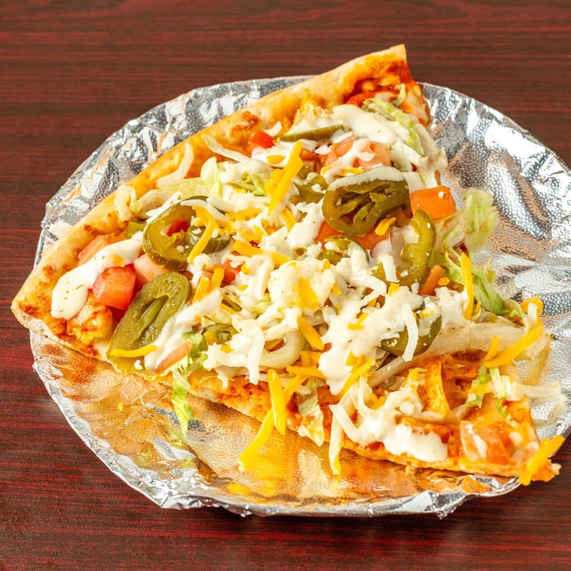 Topolino's taco pizza slice with jalapeños, tomatoes, lettuce, and cheese on foil.