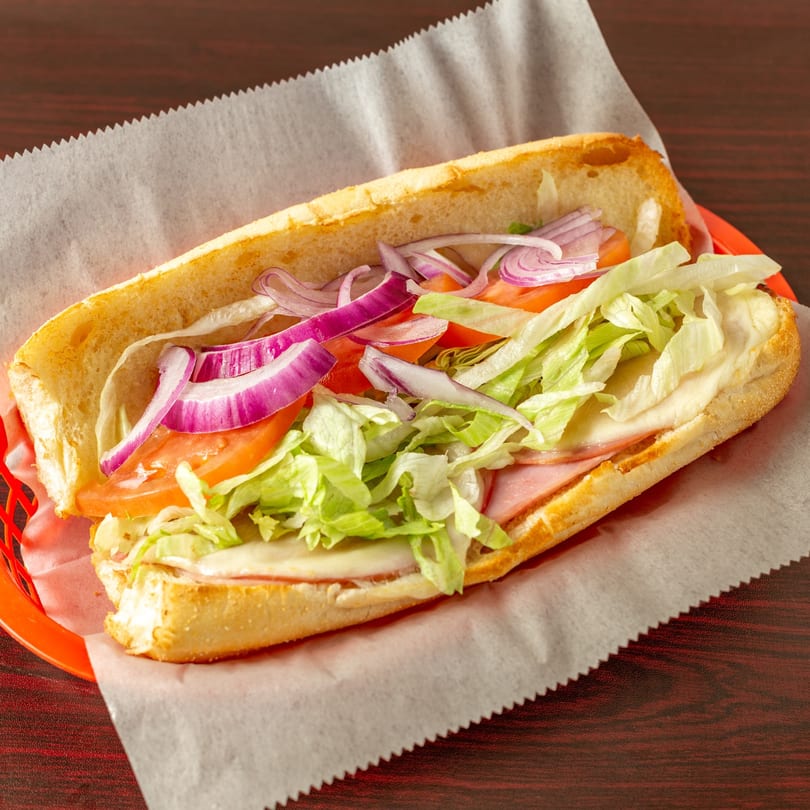 A Topolino's sub sandwich with ham, cheese, lettuce, tomatoes, and red onions in a red basket.
