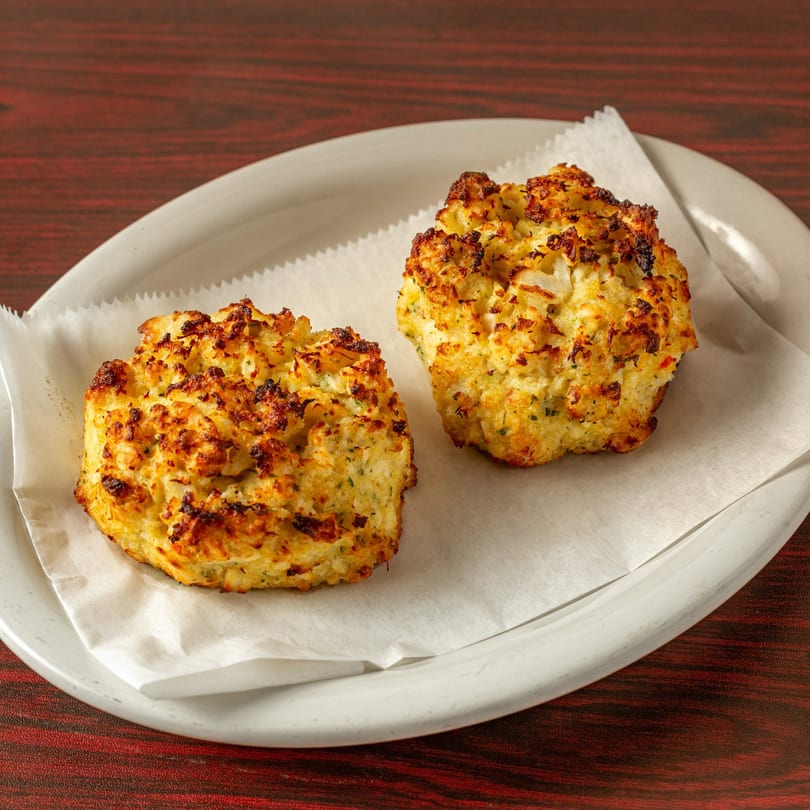 Two golden-brown Topolino's garlic knots, speckled with herbs, rest on white parchment paper on a plate.