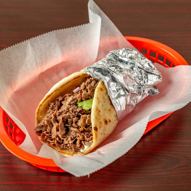 A Topolino's gyro, filled with meat, lettuce, and onions, in a red basket with foil.
