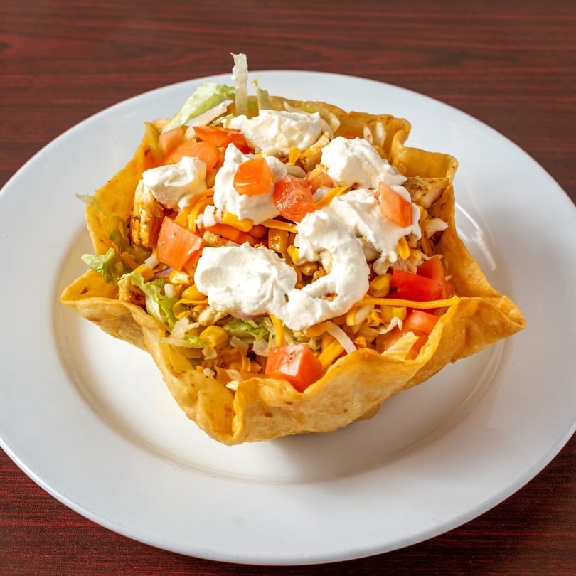 A taco salad in a crispy tortilla bowl, topped with lettuce, tomatoes, cheese, and sour cream.