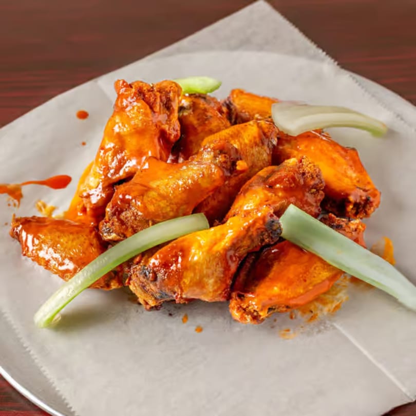 Spicy buffalo chicken wings with celery sticks on a white paper-lined plate.
